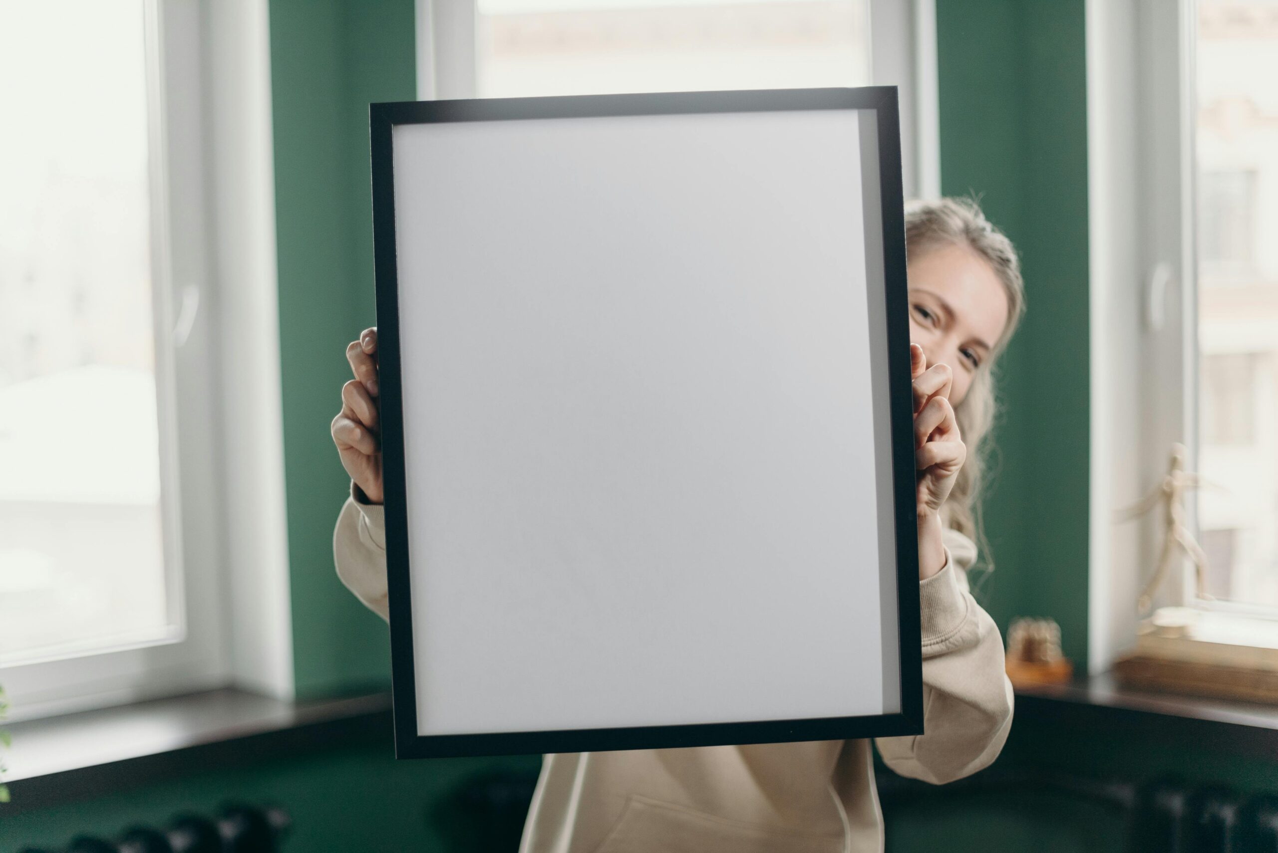 A woman indoors holding a blank photo frame, perfect for mockup or customization.