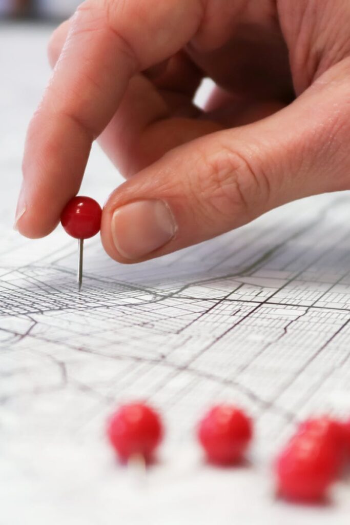 Close-up of a hand placing a red pin on a map indicating geographic location pinning.